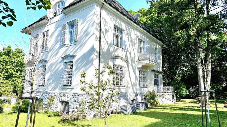 Klassische weiße Villa mit gepflegtem Garten und vielen Fenstern unter blauem Himmel.