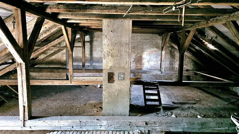 Unausgebauter Dachboden mit sichtbaren Holzbalken und Betonpfeiler, bereit für den Ausbau.