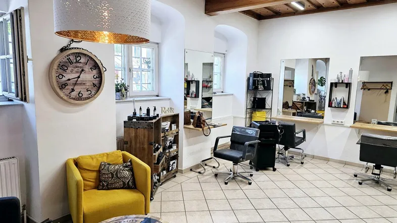 Heller Friseursalon mit hohen Decken, sichtbaren Holzbalken und modernen Einrichtungsdetails.