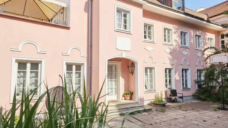 Rosa gestrichenes historisches Gebäude mit weißen Fensterrahmen und einem gepflasterten Innenhof.