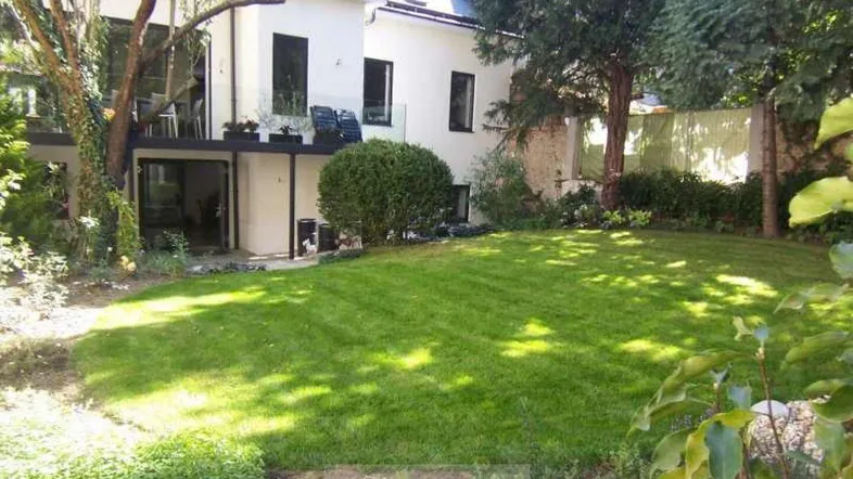 Gepflegter Garten mit großer Rasenfläche und Zugang zu einer Terrasse im Obergeschoss.