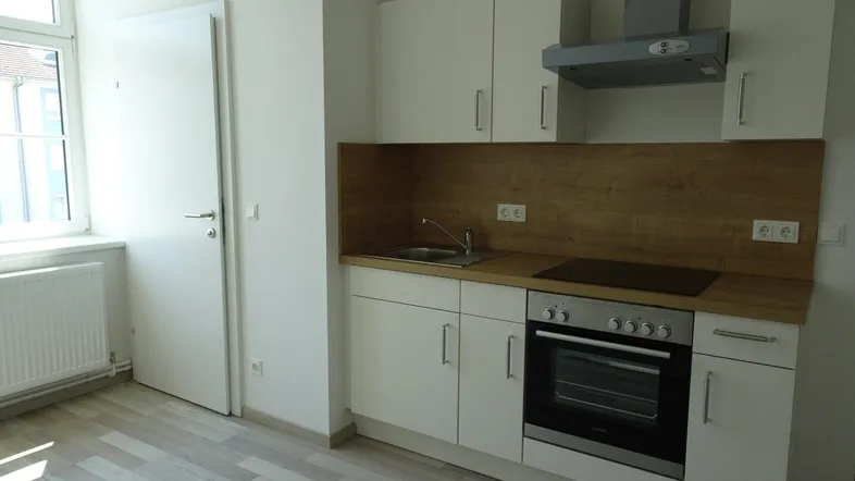 Kleine, funktionale Küche mit weißen Schränken, Holzoptik-Arbeitsplatte und Fenster für Tageslicht.