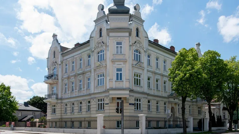 Prächtiges Eckgebäude im historischen Stil mit reich verzierten Fassaden und vielen Fenstern unter blauem Himmel.
