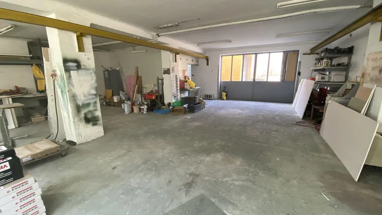 Geräumiger Werkstatt- oder Lagerbereich mit Betonboden und großen Fenstern, der Renovierungsbedarf zeigt.