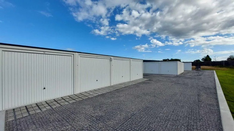Reihe moderner Garagenboxen mit weißen Toren und Schotterzufahrt unter blauem Himmel.