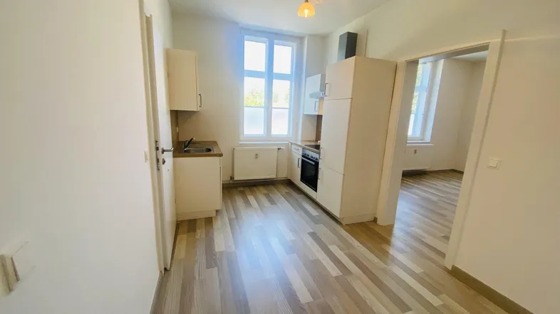 Kleine, helle Küche mit Laminatboden und Einbauschränken, offen zu einem weiteren Raum.