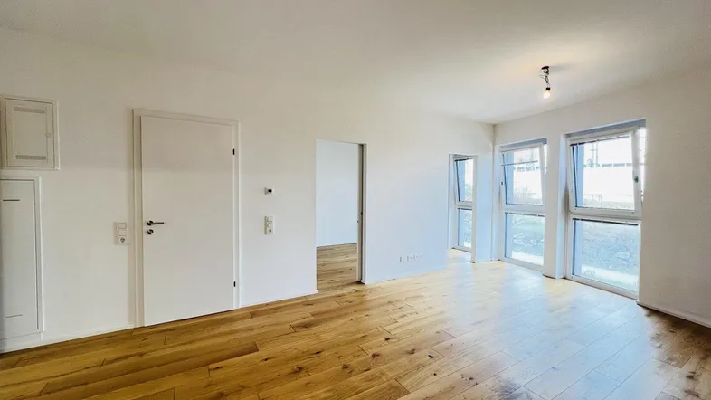 Helles, leeres Zimmer mit schönen Holzböden und großen Fenstern, bereit zur individuellen Gestaltung.