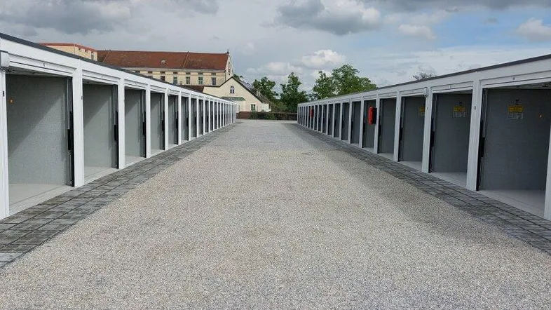 Lange Reihen von neuen Garagenboxen mit offenen Toren und einem Schotterweg unter bewölktem Himmel.