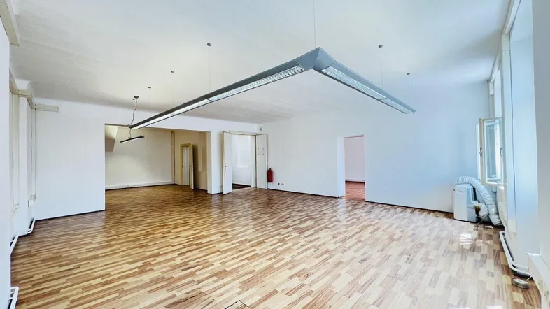 Großer, heller Büroraum mit Holzparkettboden und mehreren Türen, ausgestattet mit modernen Deckenleuchten.