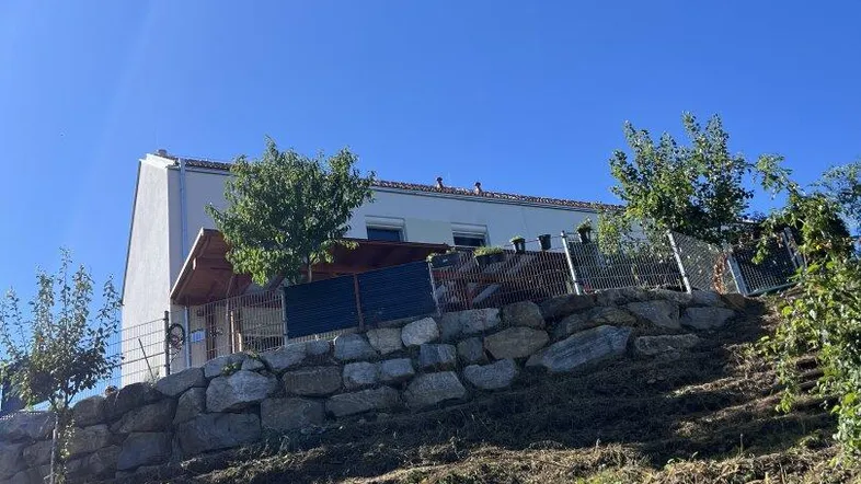 Weißes Wohnhaus auf einem Hanggrundstück mit Terrassenbereich und viel Grün.