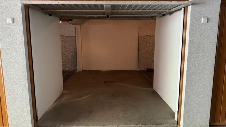 Einfahrt zu einer einzelnen Garage mit Betonboden, weißen Wänden und seitlichen Gitterabtrennungen.