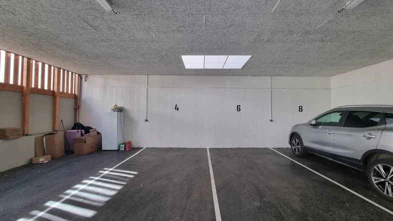 Geräumige Tiefgarage mit einem geparkten Auto, gekennzeichneten Stellplätzen und Lagerbereich.