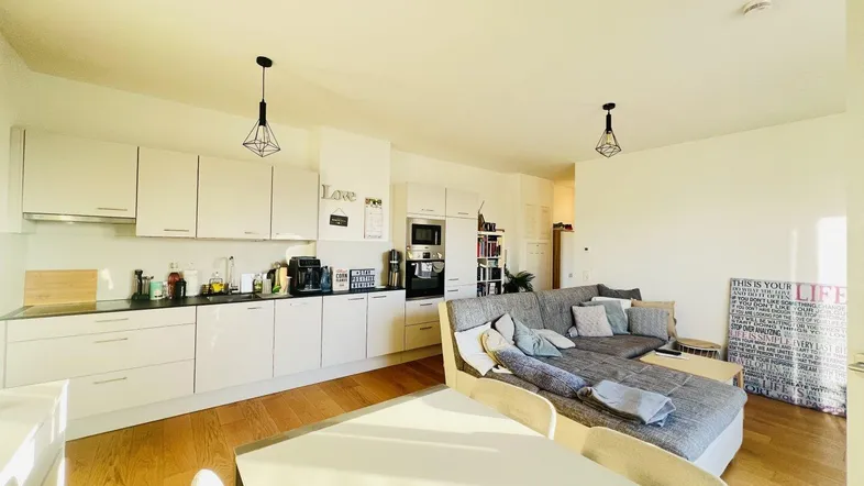 Heller offener Wohn- und Essbereich mit moderner Küche, Holzboden und gemütlichem Sofa.