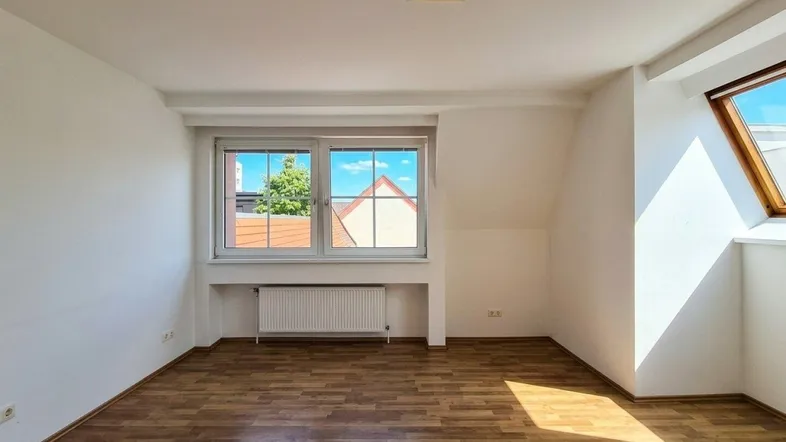 Helles Zimmer mit Laminatboden, zwei Fenstern und Dachschräge, gut beleuchtet durch Tageslicht.