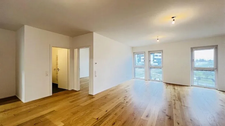 Heller, leerer Raum mit hochwertigem Holzboden und großen Fenstern, die viel Tageslicht hereinlassen.