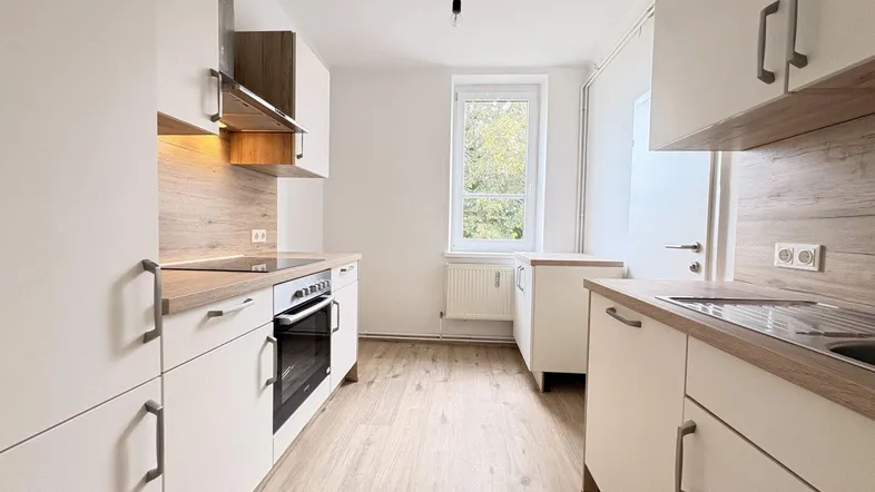 Helle, moderne Küche mit weißen Schränken, Holzakzenten und Fensterblick ins Grüne.