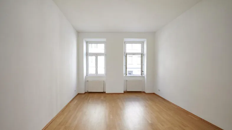 Heller, leerer Raum mit Parkettboden und zwei großen Fenstern, bereit zur individuellen Gestaltung.