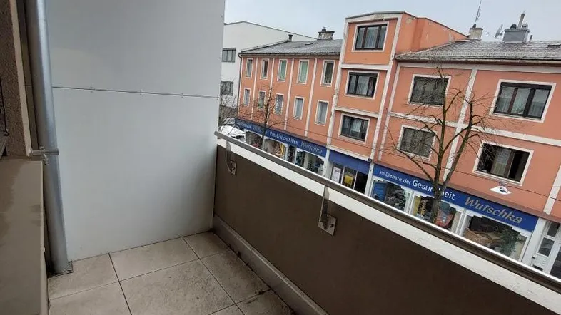 Kleiner Balkon mit Fliesenboden und Blick auf die belebte Straße und gegenüberliegende Gebäude.
