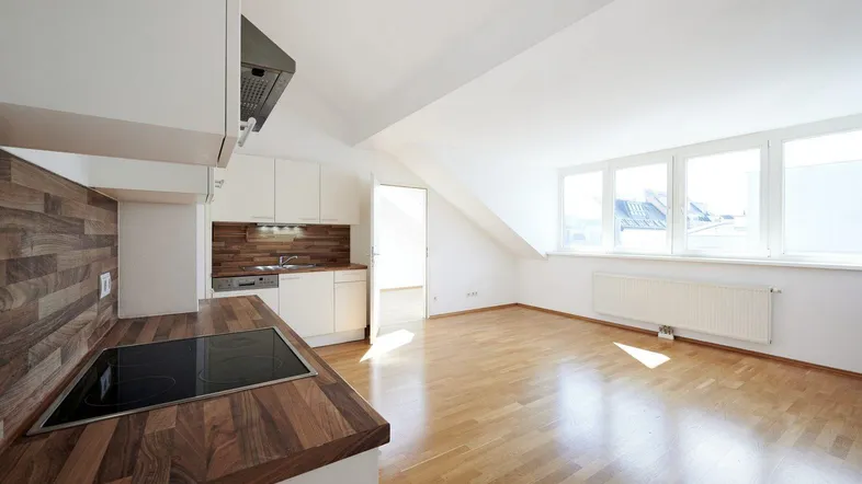Helle Dachgeschosswohnung mit offener Küche, Holzarbeitsplatte und Parkettboden.