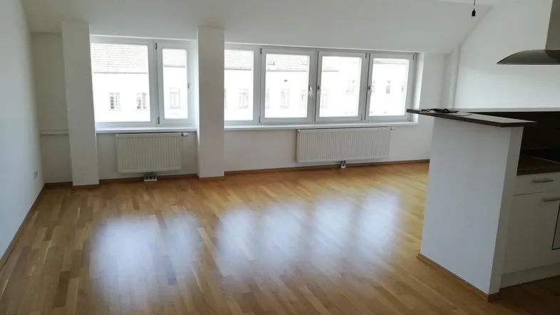 Helles Wohnzimmer mit Parkettboden, großen Fenstern und offener Küchenzeile.