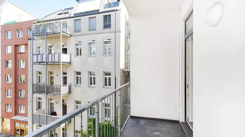 Heller Balkon mit Fliesenboden und Blick auf die umliegenden Gebäude und den Innenhof.