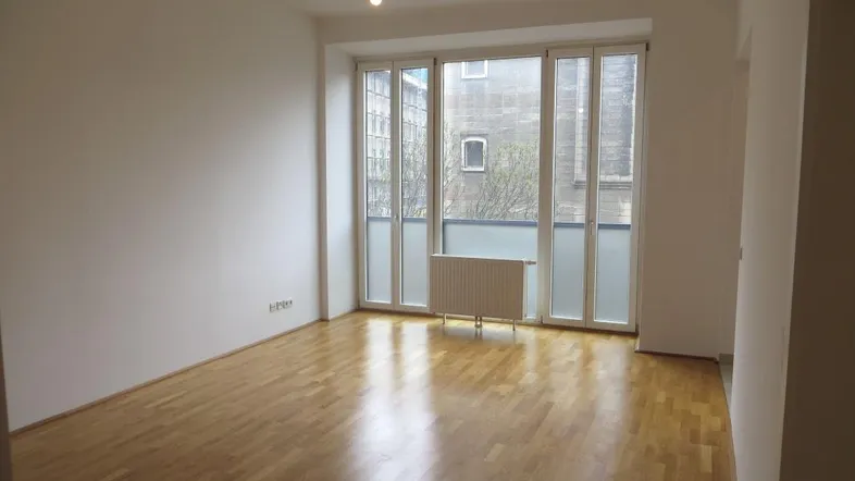 Helles Zimmer mit Parkettboden und großen Fenstern, die viel Tageslicht hereinlassen.