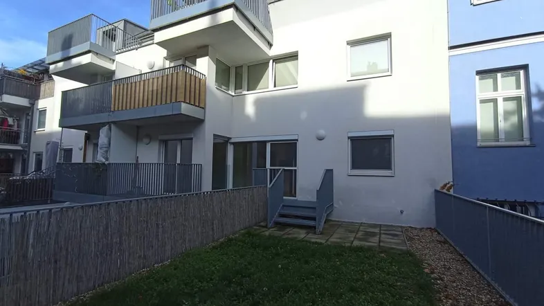 Kleiner privater Gartenbereich mit Rasenfläche und gepflasterter Terrasse hinter dem Gebäude.