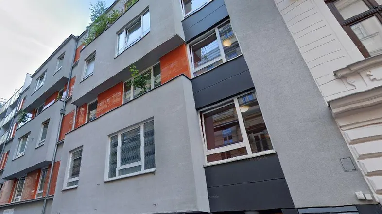 Moderne Fassade eines Wohngebäudes mit grauen und orangefarbenen Akzenten und großen Fenstern.