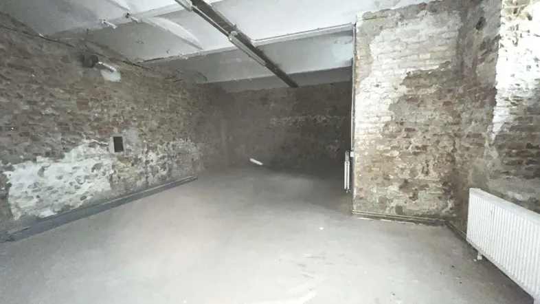 Leerer Raum mit unverputzten Ziegelwänden, Betonboden und sichtbaren Deckenbalken, bereit für den Ausbau.