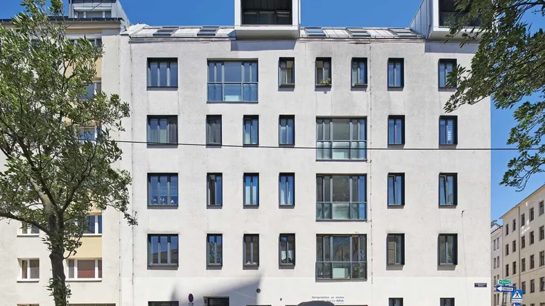 Moderne Wohnhausfassade mit zahlreichen Fenstern und Dachaufbauten unter blauem Himmel.