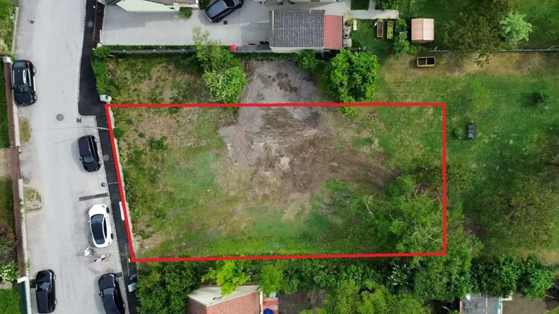 Luftaufnahme eines Baugrundstücks mit roter Umrandung, umgeben von Wohnhäusern und einer Straße.