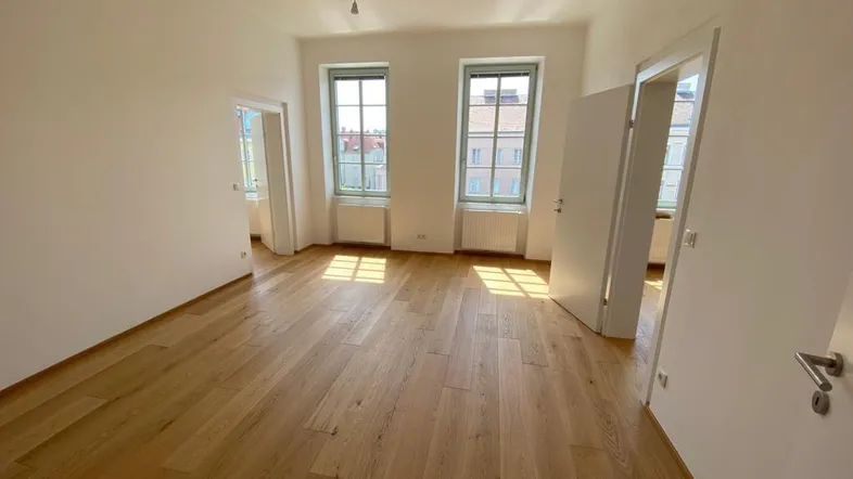 Helles Zimmer mit neuem Parkettboden und großen Fenstern, das viel Tageslicht hereinlässt.