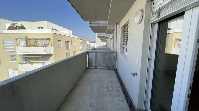 Langer, schmaler Balkon mit Betonboden und Blick auf umliegende Gebäude.