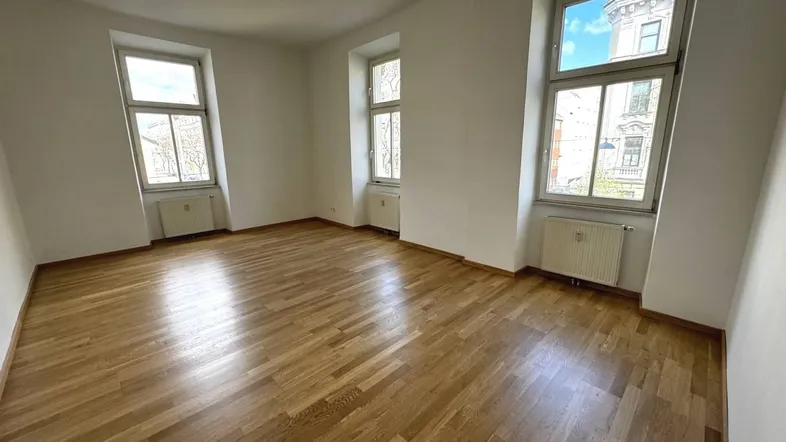 Helles Zimmer mit Parkettboden und mehreren Fenstern, ideal als Wohn- oder Schlafzimmer nutzbar.