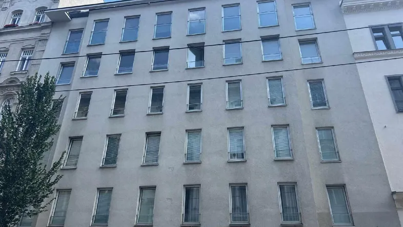 Moderne Fassade eines Mehrfamilienhauses mit vielen Fenstern und Werbeschildern im Stadtgebiet.