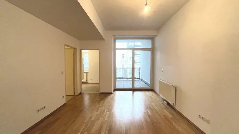 Helles Zimmer mit Parkettboden und Zugang zu einem Balkon, ideal als Wohn- oder Schlafbereich.