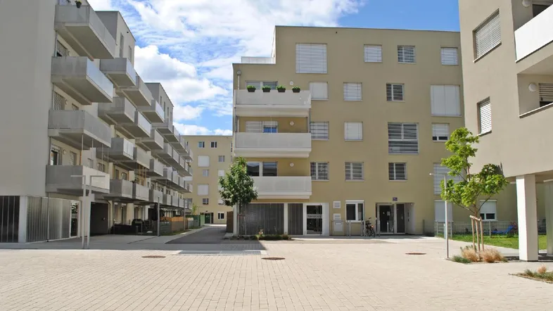 Moderne Wohngebäude mit Balkonen und einem gepflasterten Innenhof unter blauem Himmel.