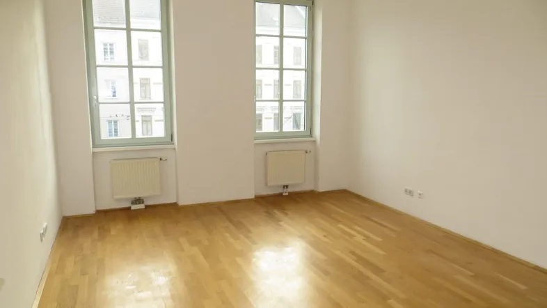 Heller Raum mit Parkettboden und zwei großen Fenstern, ideal als Wohn- oder Schlafzimmer.