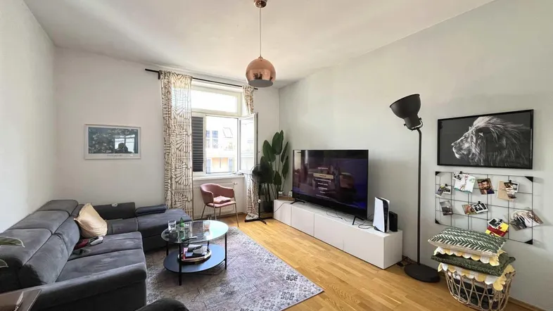 Helles Wohnzimmer mit modernem Sofa, Holzboden und einem Fenster, das viel Tageslicht hereinlässt.