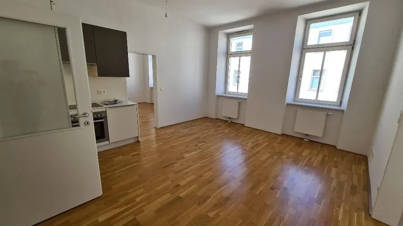 Helles Wohnzimmer mit Parkettboden und integrierter Küchenzeile, ideal für offenes Wohnen.