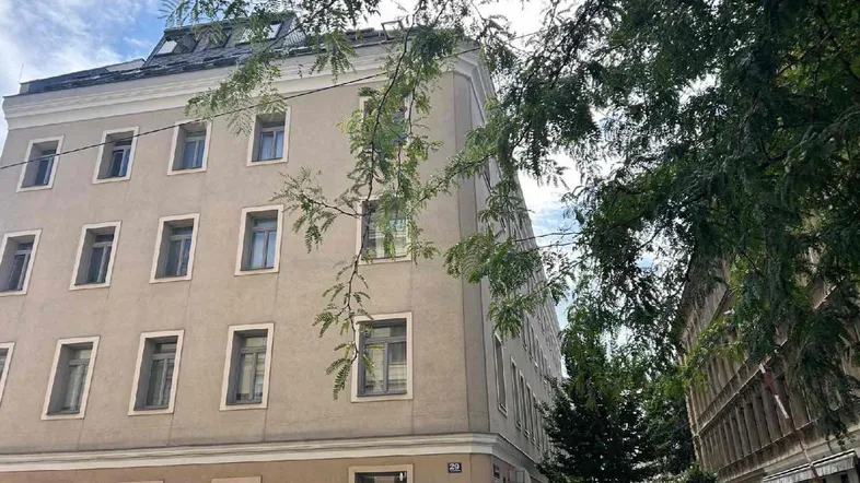 Das Gebäude präsentiert sich mit einer hellen Fassade und mehreren Fenstern in einer städtischen Umgebung.