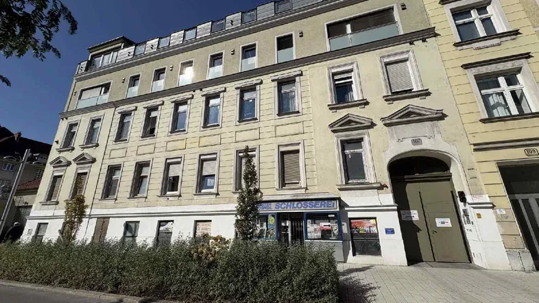 Fassade eines Mehrfamilienhauses mit Geschäften im Erdgeschoss unter blauem Himmel.
