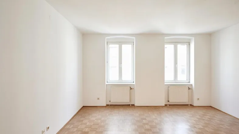 Helles, leeres Zimmer mit Parkettboden und zwei Fenstern, bereit zur individuellen Gestaltung.