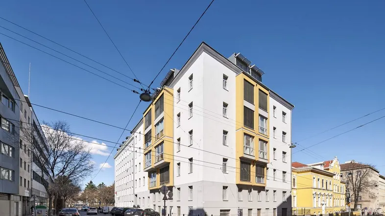 Modernes Mehrfamilienhaus mit weißer Fassade und gelben Akzenten an den Fensterfronten.