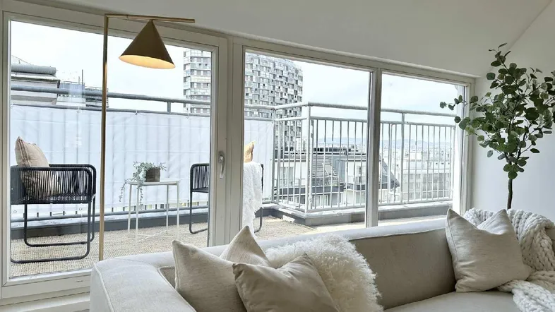 Helles Wohnzimmer mit beigem Sofa, modernen Möbeln und Zugang zu einem Balkon mit Stadtblick.