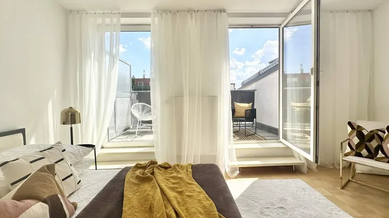 Helles Schlafzimmer mit Zugang zu einem Balkon und moderner Einrichtung sowie viel Tageslicht.