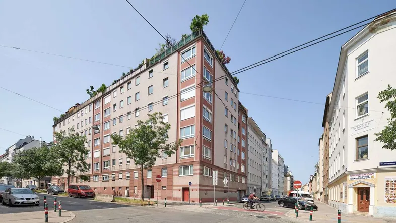 Mehrstöckiges Wohngebäude an einer Straßenecke mit begrüntem Flachdach und vielen Fenstern.