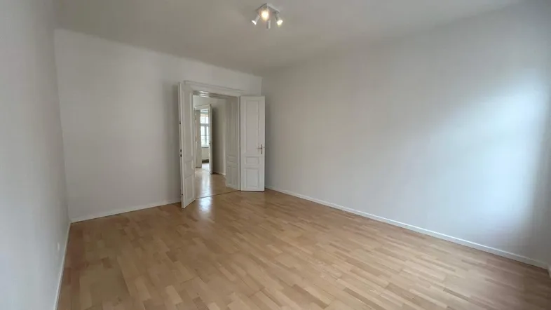 Helles, leeres Zimmer mit Parkettboden und weiß gestrichenen Wänden, bereit zur individuellen Gestaltung.