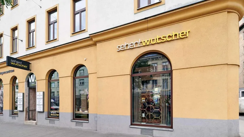 Nahaufnahme der Gebäudefassade mit großen Rundbogenfenstern und einem Ladengeschäft im Erdgeschoss.