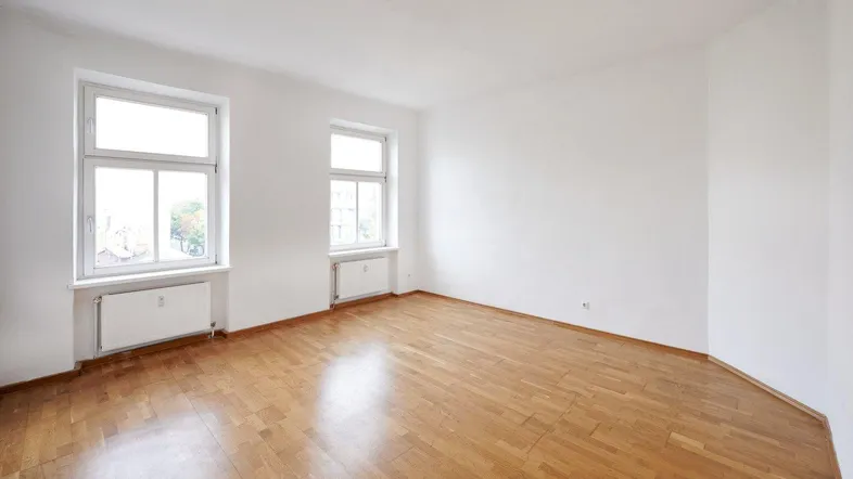 Helles Zimmer mit Parkettboden und zwei Fenstern, ideal als Wohn- oder Schlafzimmer nutzbar.